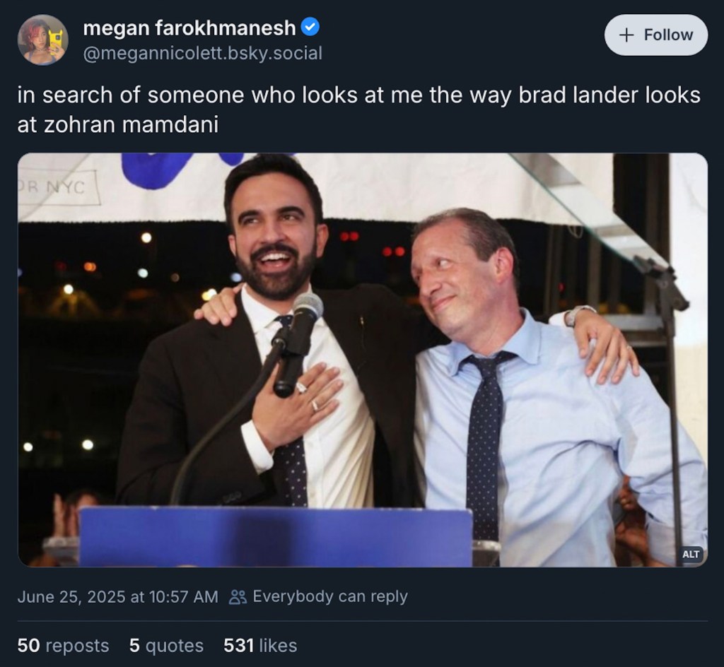 A joyful moment between two men at a public event, one speaking into a microphone and the other smiling and embracing him, with a backdrop of city lights.